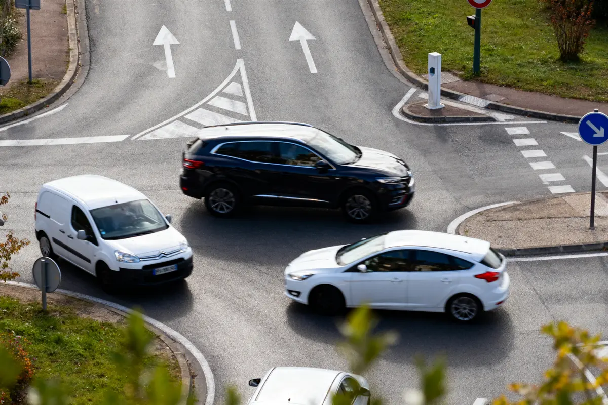 Trois voitures circulent dans un rond-point bien balisé avec flèches directionnelles et signalisation.