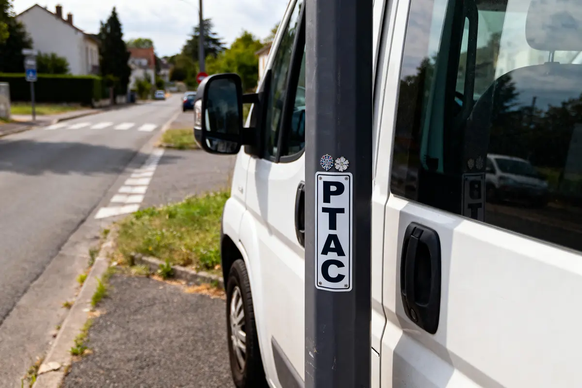 Camionnette blanche stationnée près d'un panneau "PTAC" sur une rue résidentielle avec passage piéton.