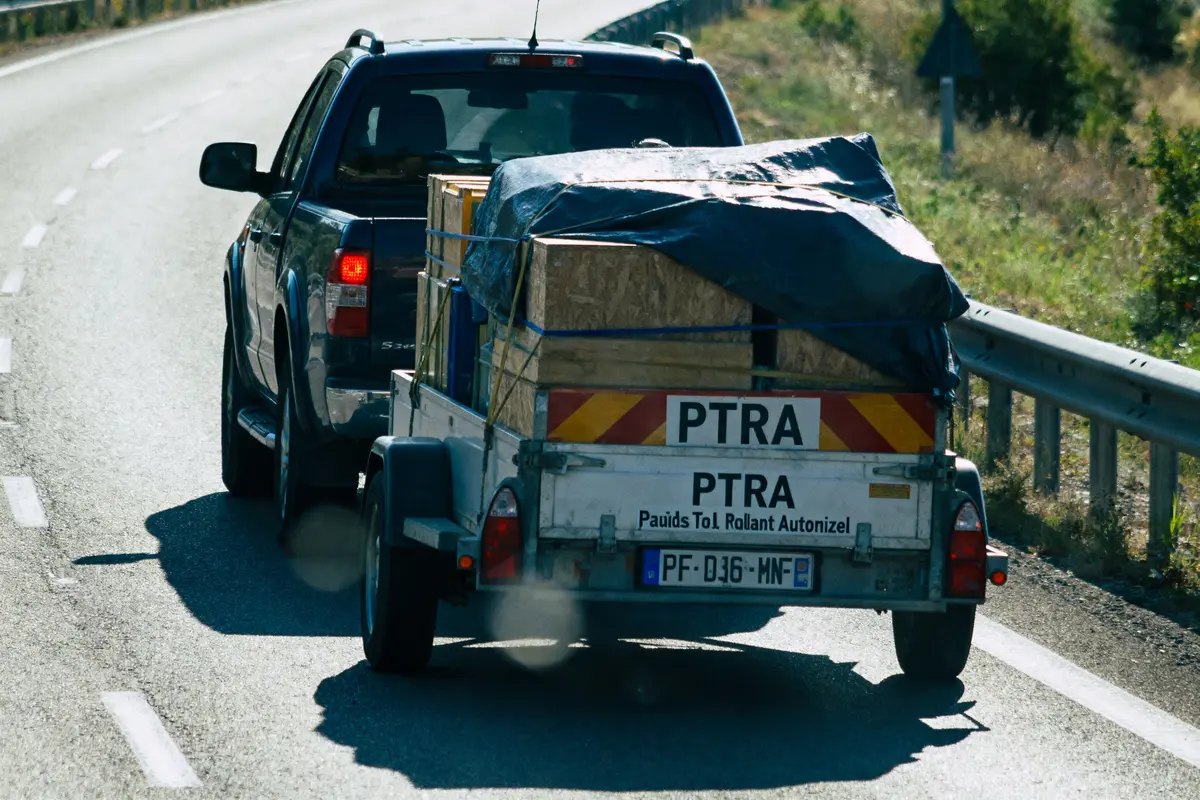 Pickup avec remorque sur route, transportant une caisse couverte de bâche bleue.
