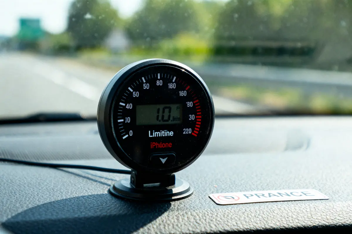 Appareil de mesure circulaire sur tableau de bord de voiture, affichant 1.0, avec route floue en arrière-plan.