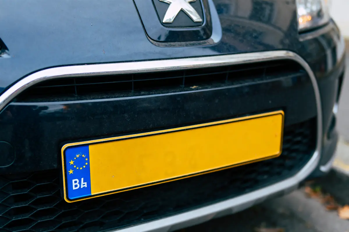 Plaque d'immatriculation européenne jaune sur voiture noire, avant Peugeot. Symbole UE et "В4" visibles.