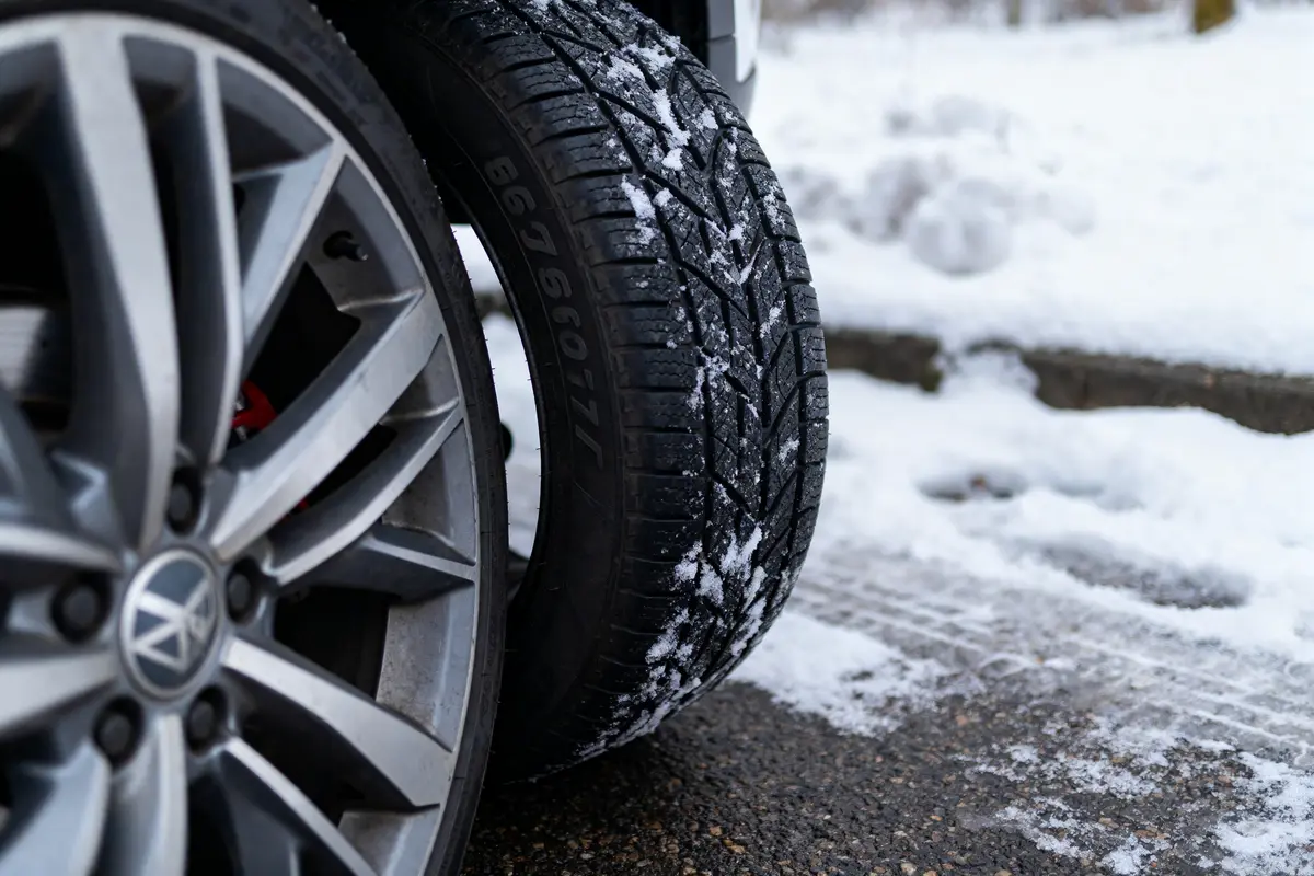 Pneus de voiture sur route enneigée, avec jantes métalliques et neige fondant partiellement sur l'asphalte.