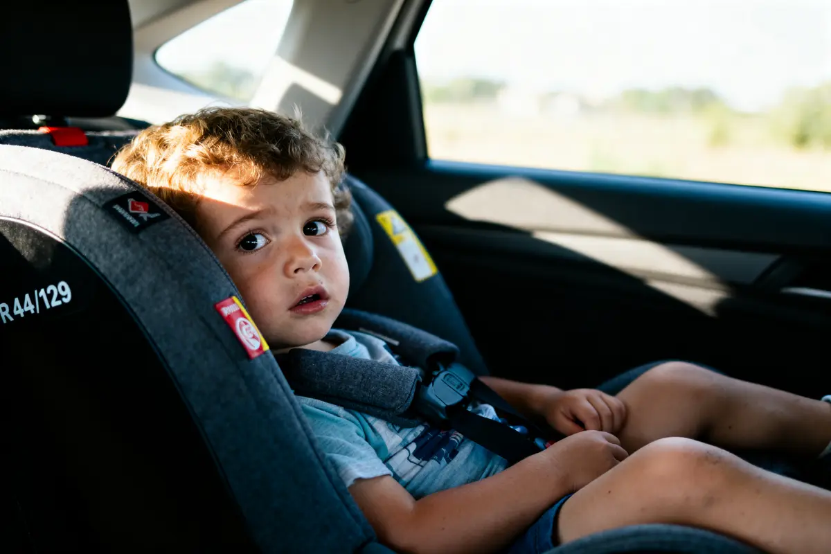 Enfant assis dans un siège auto, regard interrogatif, éclairé par la lumière du jour, intérieur de la voiture.