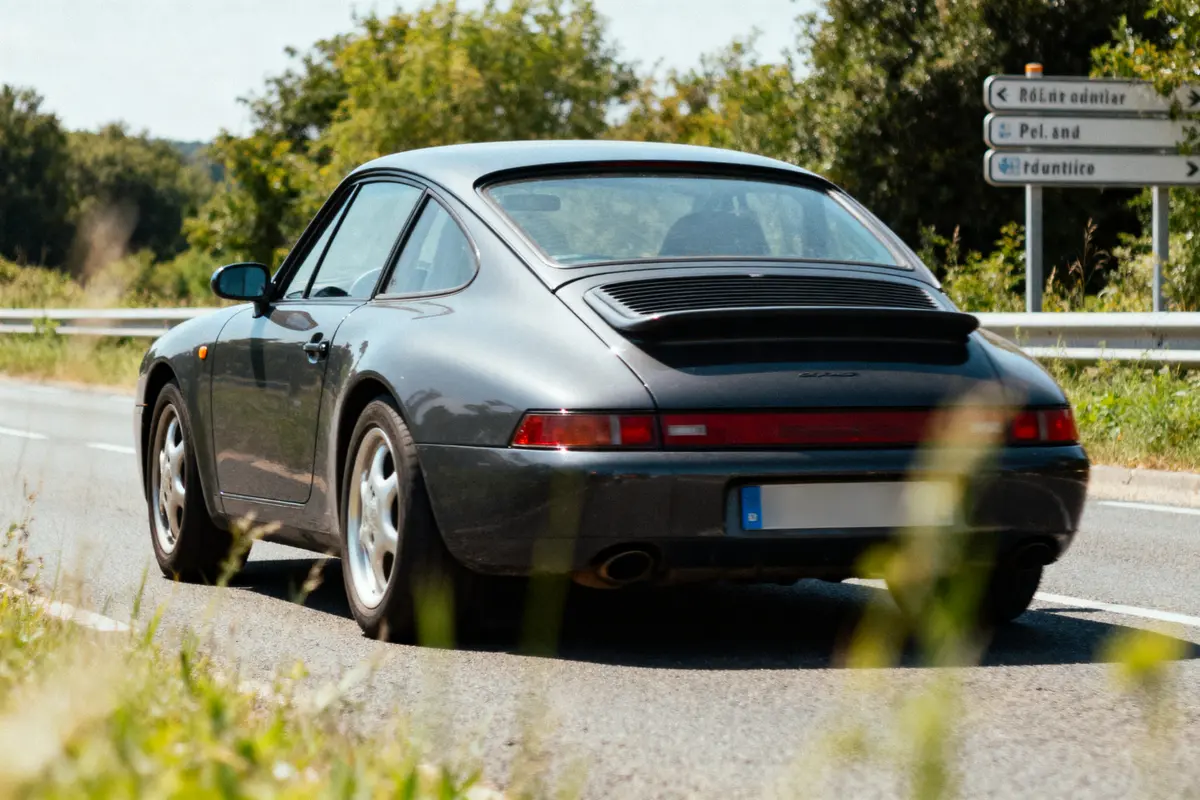 Voiture noire sur route de campagne, panneaux de signalisation en arrière-plan, journée ensoleillée.