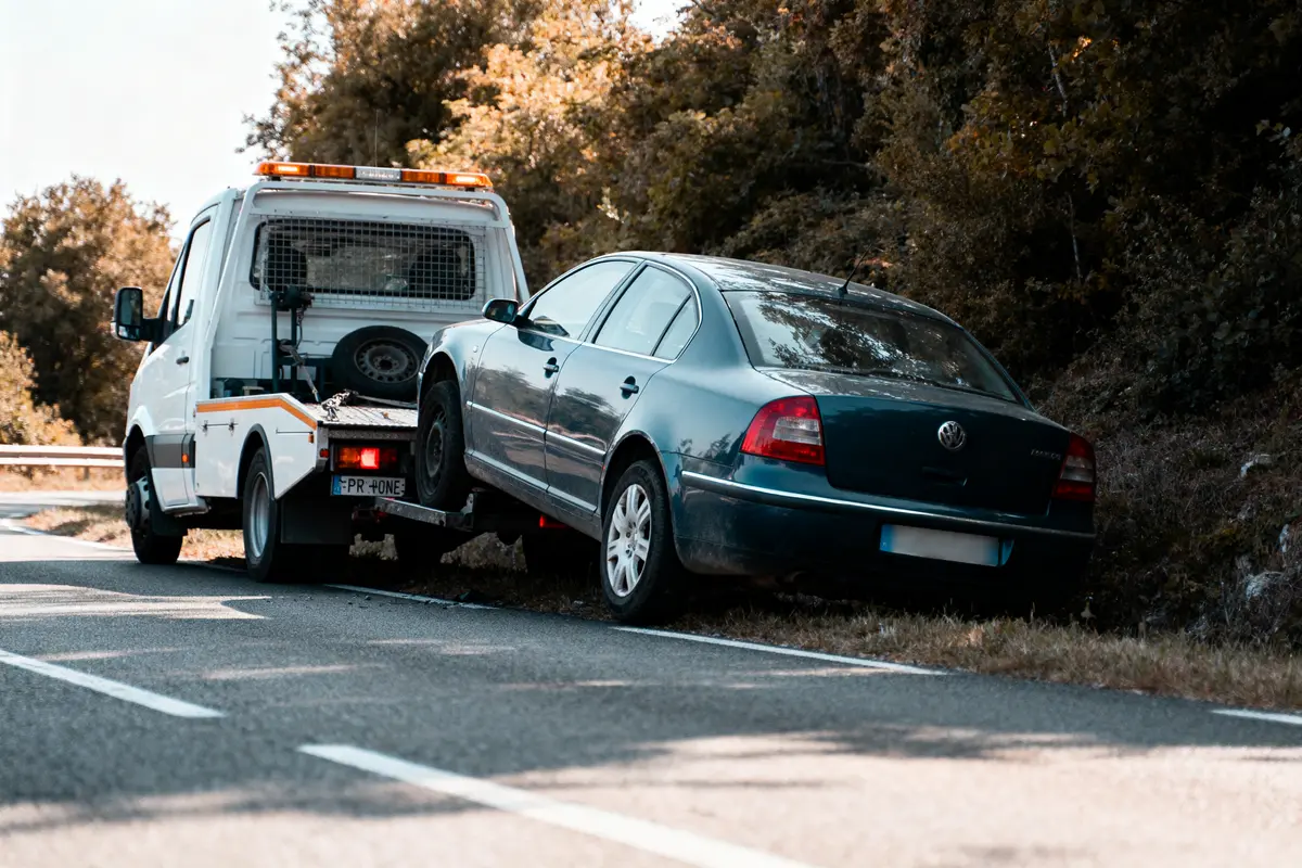Une dépanneuse remorque une voiture accidentée sur le bord de la route, entourée de végétation.