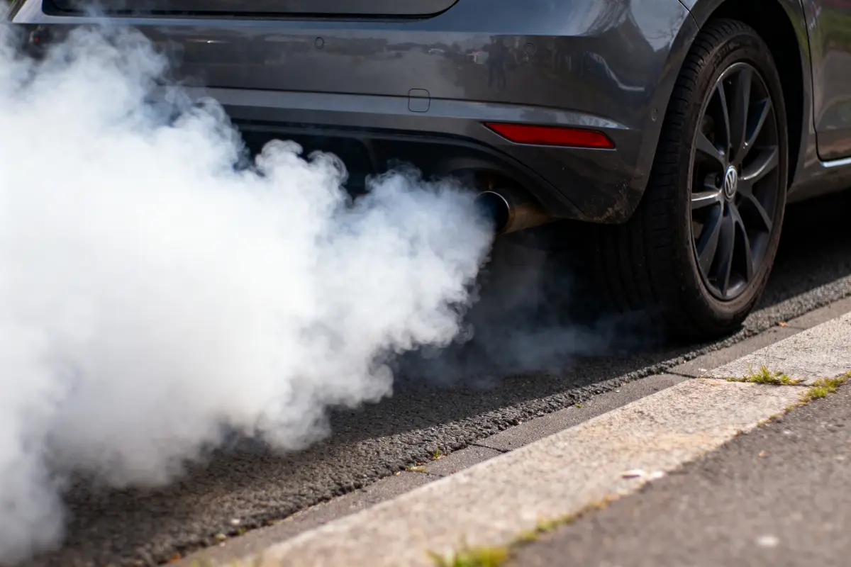Voiture grise émettant fumée blanche dense par l'échappement, stationnée sur la route.
