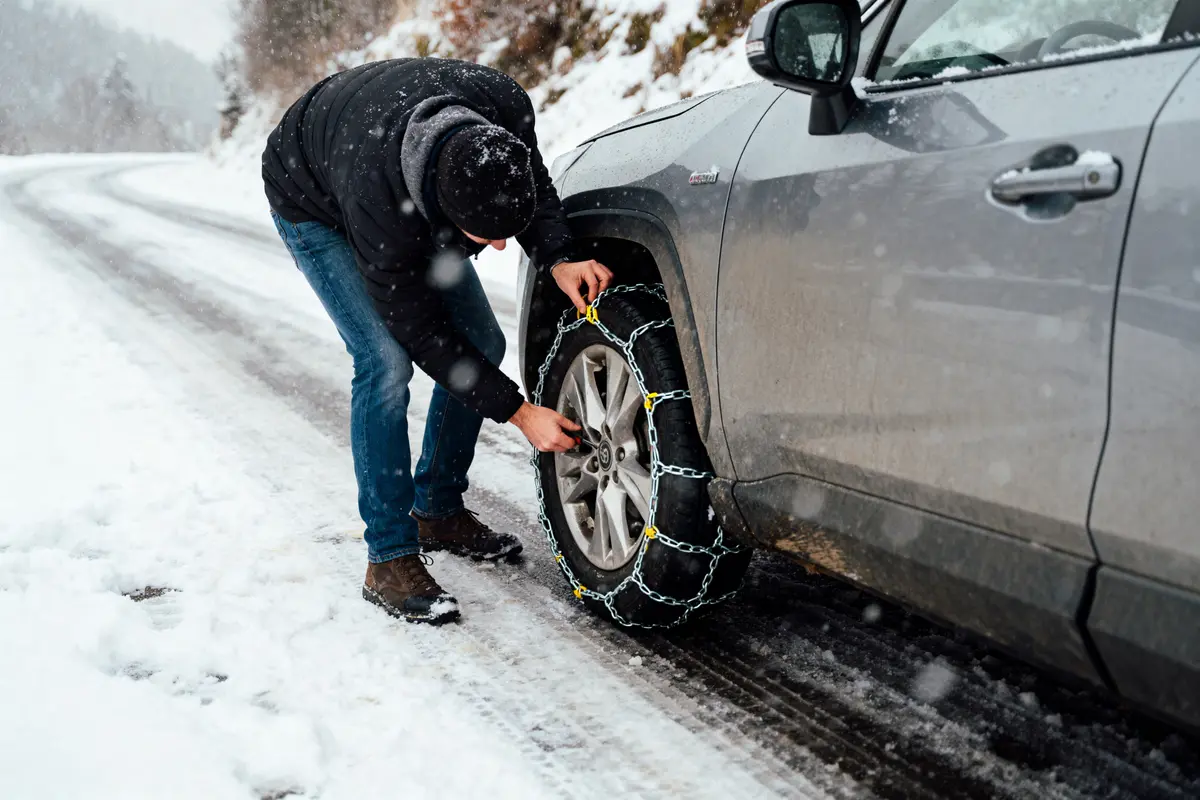 Personne installant des chaînes à neige sur un pneu de voiture par temps neigeux sur une route glissante.