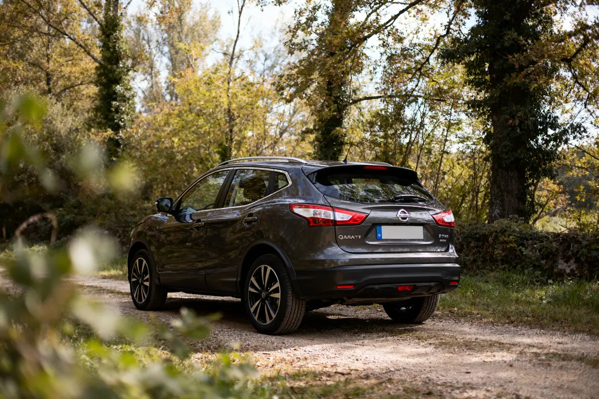 SUV gris stationné sur chemin forestier, arbres verts et feuillage en arrière-plan, illuminé par la lumière naturelle.