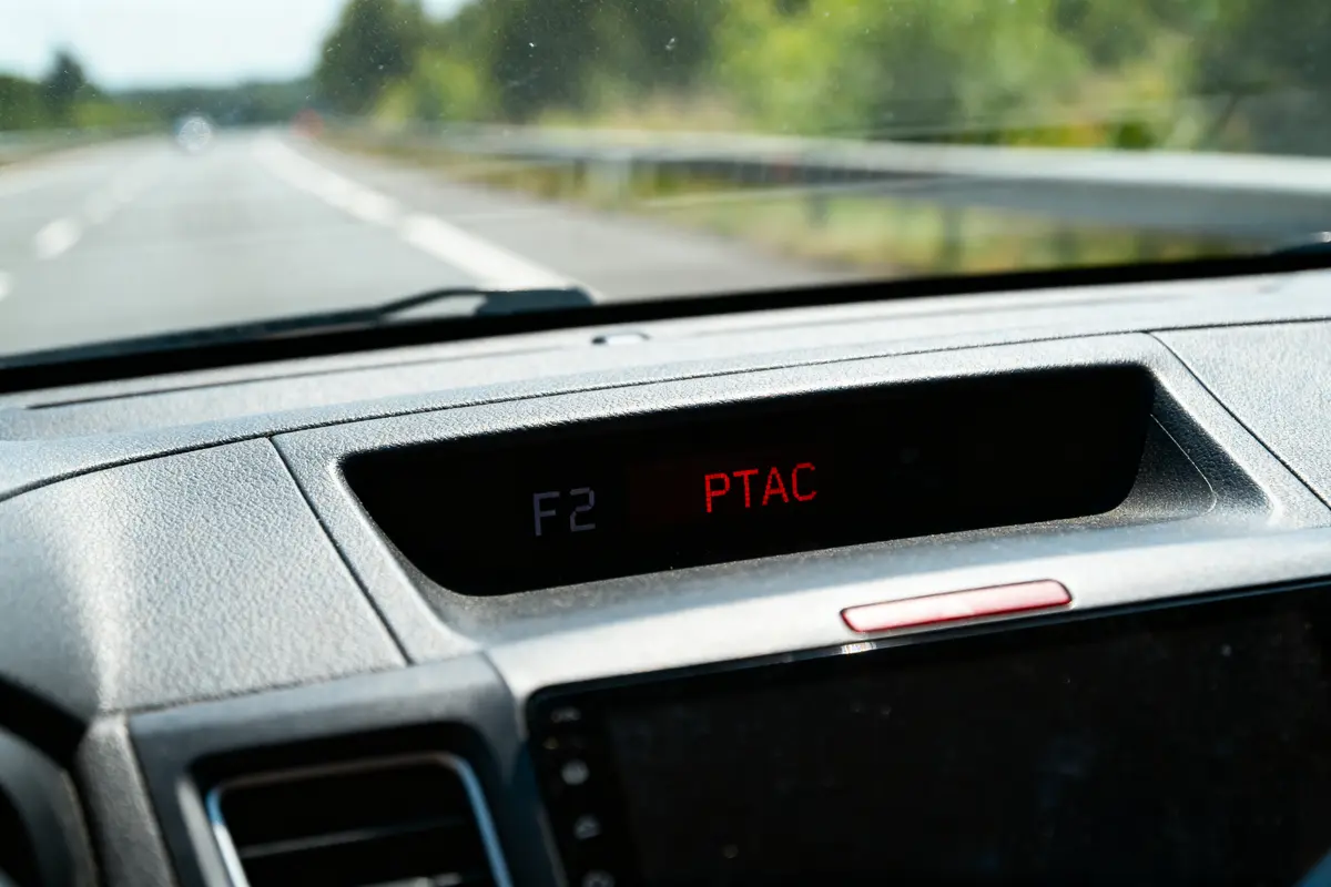 Tableau de bord d'un véhicule affichant "F2 PTAC" sur la route ensoleillée.