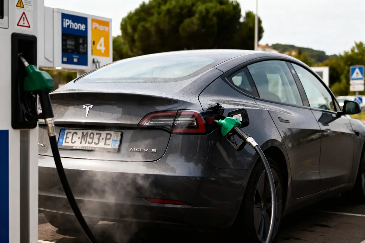 Voiture électrique Tesla remplie de carburant à une station-service, pompe avec tuyau vert.