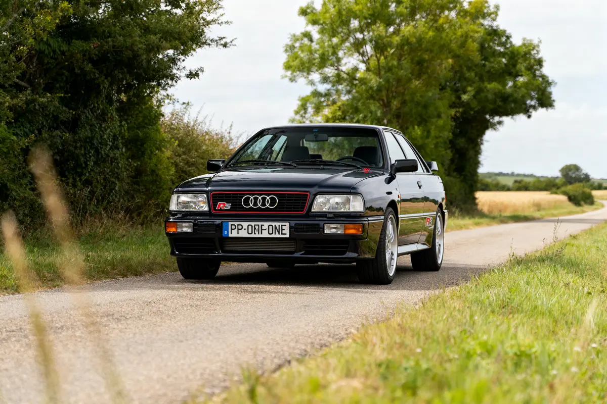 Audi RS2 Avant noire sur une route de campagne verdoyante en été
