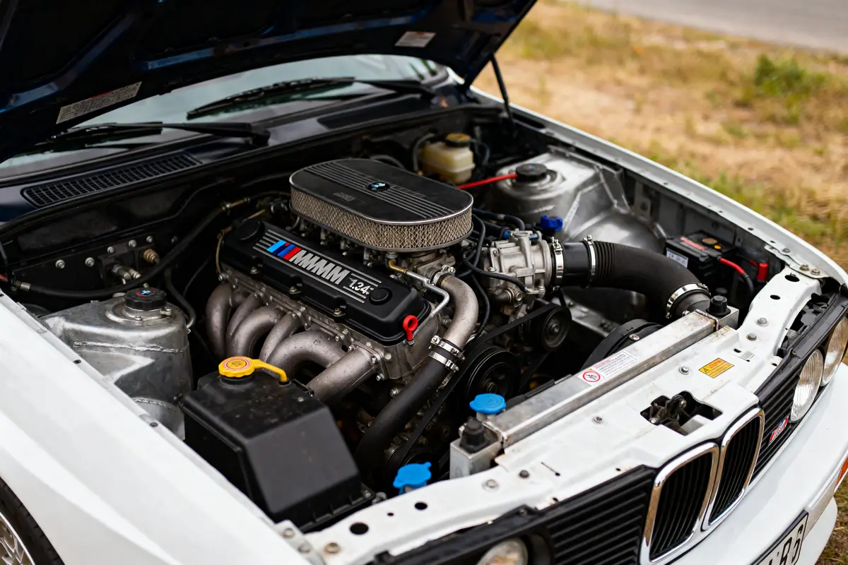 Moteur performant de BMW M3 E30 avec capot levé et vue détaillée du moteur