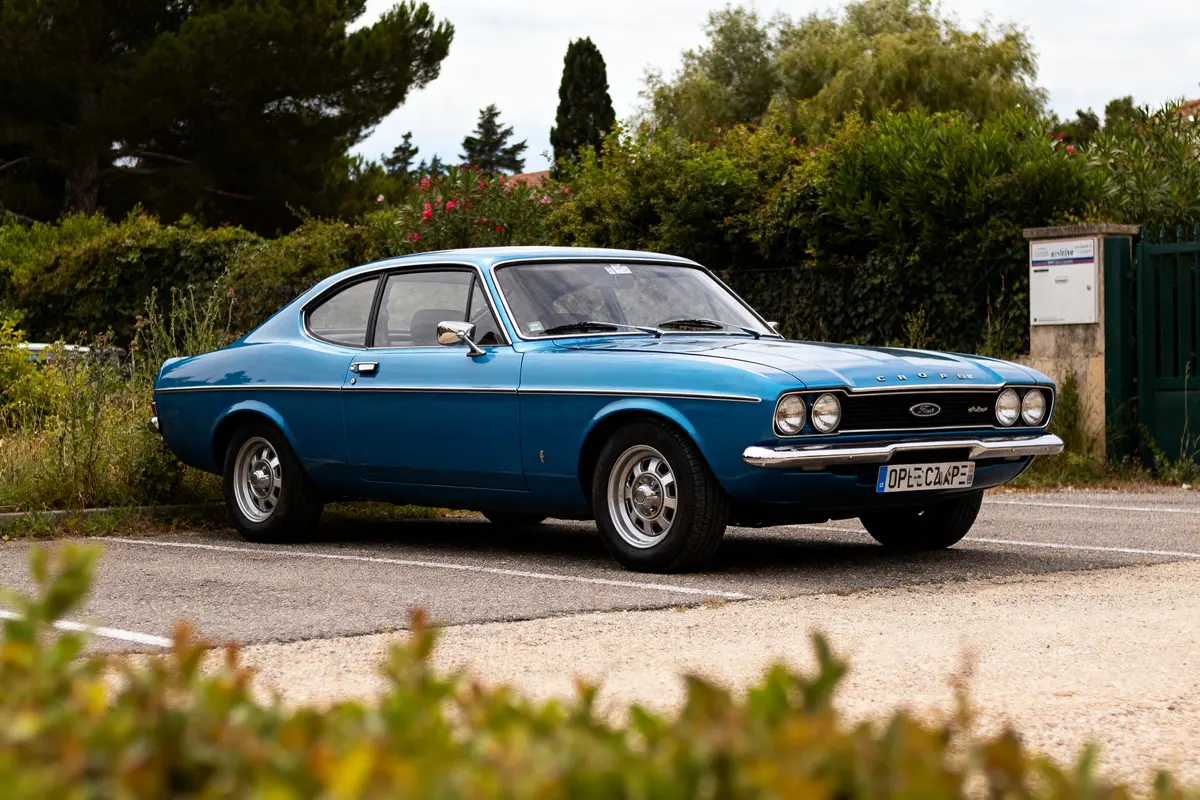 Voiture classique bleue Ford Capri 1970 garée devant un jardin verdoyant