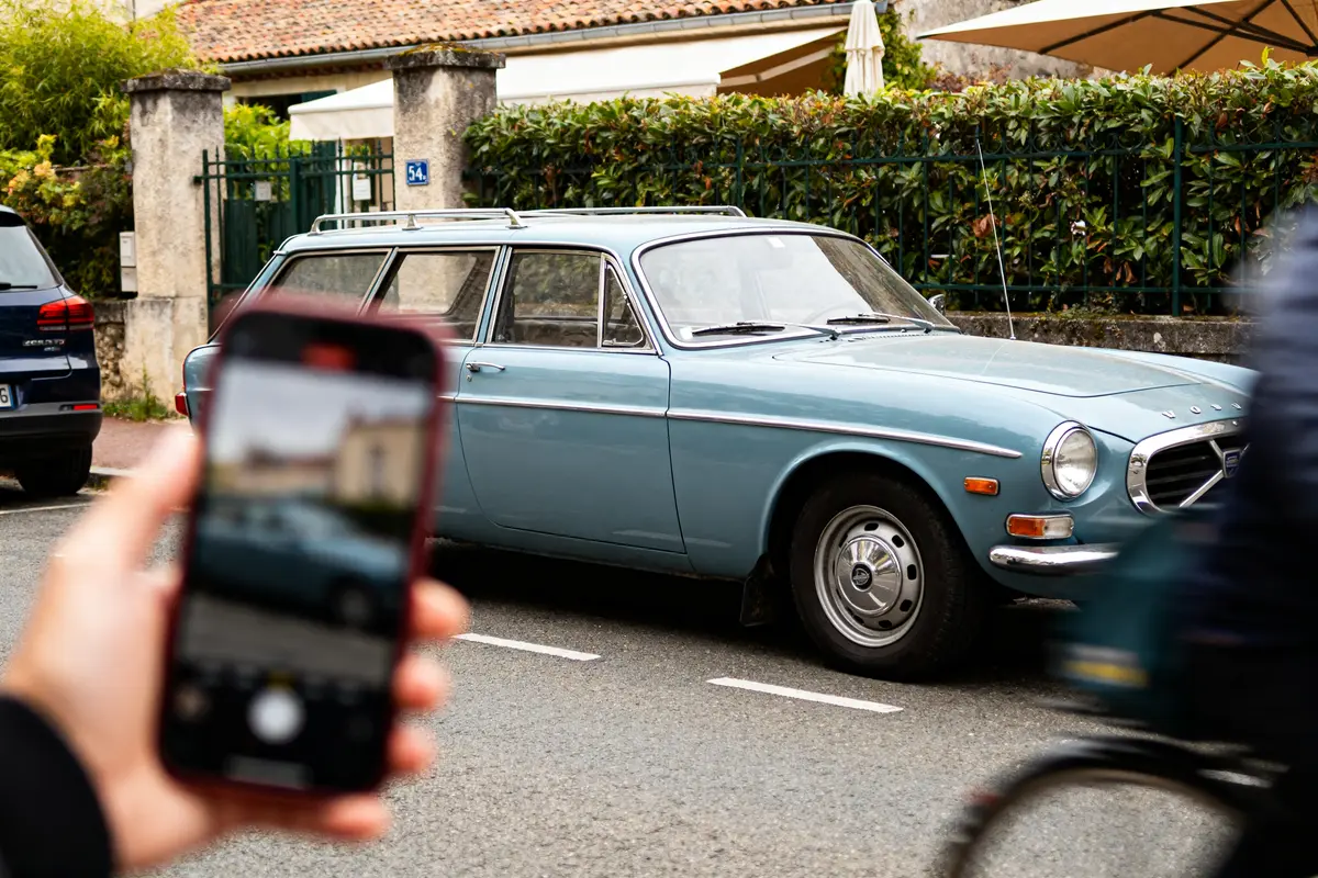 Personne prenant en photo une P1800 Volvo wagon stationnée dans une rue résidentielle